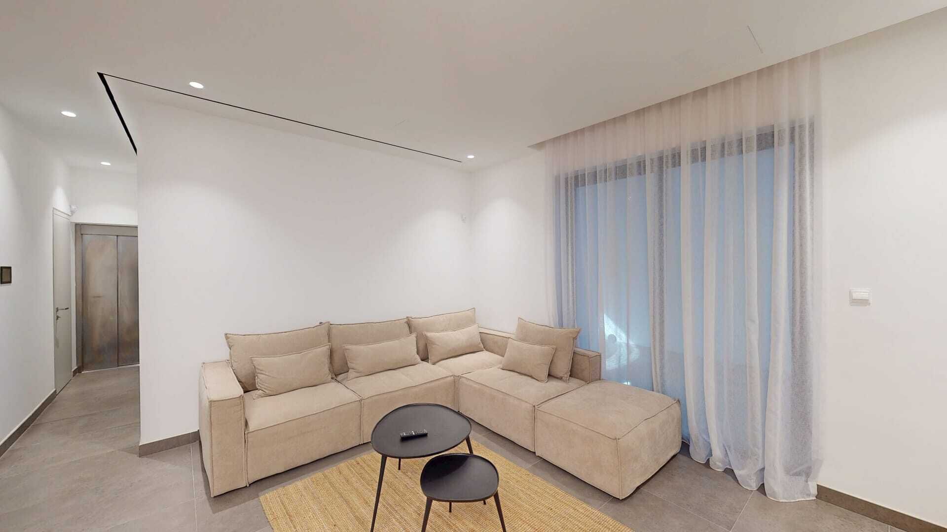 A modern living room with a sectional sofa, a small table, and a large window with sheer curtains.