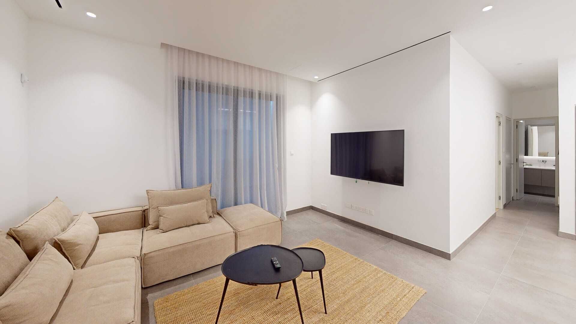 Un salon moderne avec un canapé, un téléviseur à écran plat fixé au mur et une petite table avec des chaises.