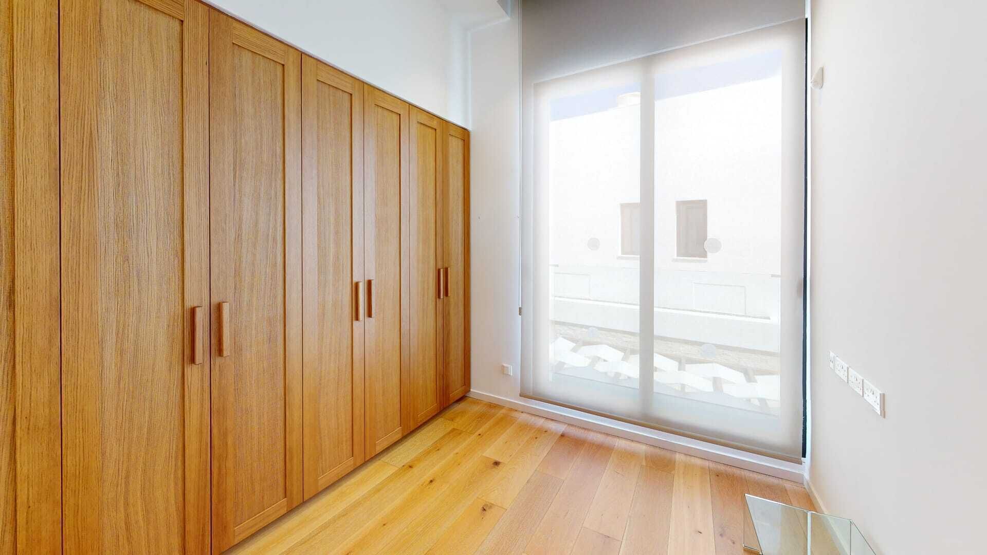 Une pièce dotée d’un plancher en bois, d’une porte-fenêtre coulissante et d’une grande armoire.