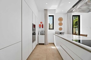 A modern kitchen with white cabinetry, a built-in oven, a coffee machine, and a window with a view of greenery. - Escape to Coastal Comfort | Villa 1030 (Famagusta)