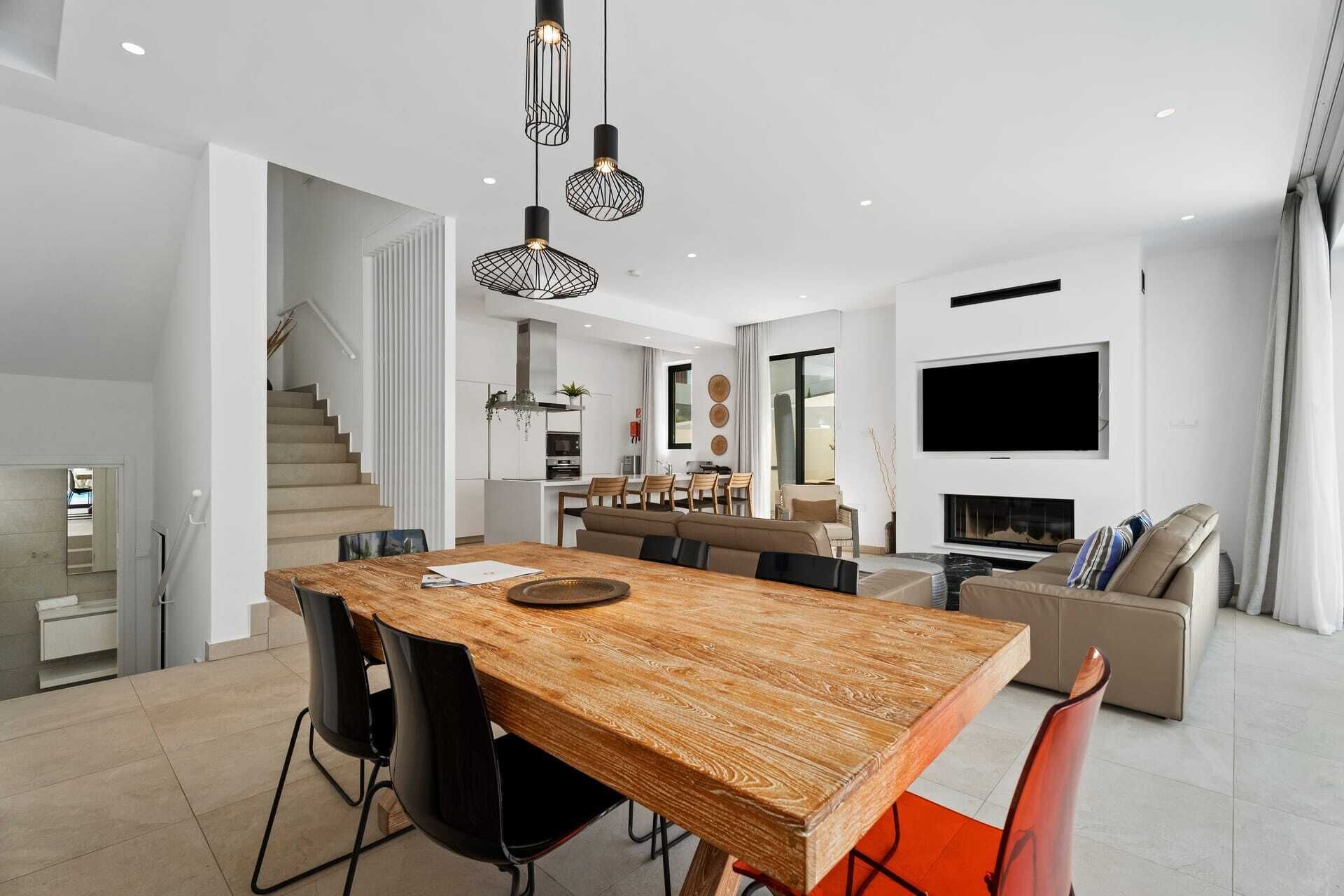 Ein modernes Interieur mit einem Holzesstisch, schwarzen Stühlen, einer Couch und einem an der Wand befestigten Fernseher.