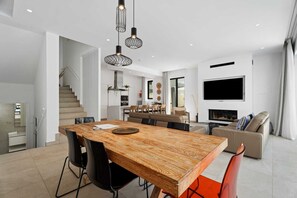 A modern interior with a wooden dining table, black chairs, a sofa, and a TV mounted on the wall.