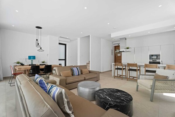 A modern living room with a sofa, ottoman, and dining area with chairs and a table.