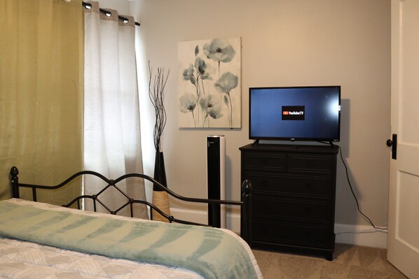 A bedroom with a bed, a dresser, a television on top of the dresser, and a painting on the wall.