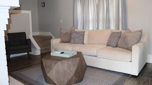 Uma sala de estar com sofá, mesa de centro, poltrona e escada.