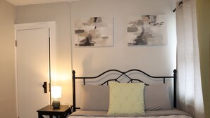 Quarto com uma cama, uma mesa de cabeceira com abajur e duas pinturas abstratas na parede.