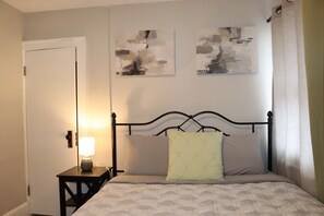 A bedroom with a bed, a nightstand with a lamp, and two abstract paintings on the wall. - 3-bedroom house in phenomenal Columbus with cool AC breeze (Columbus)