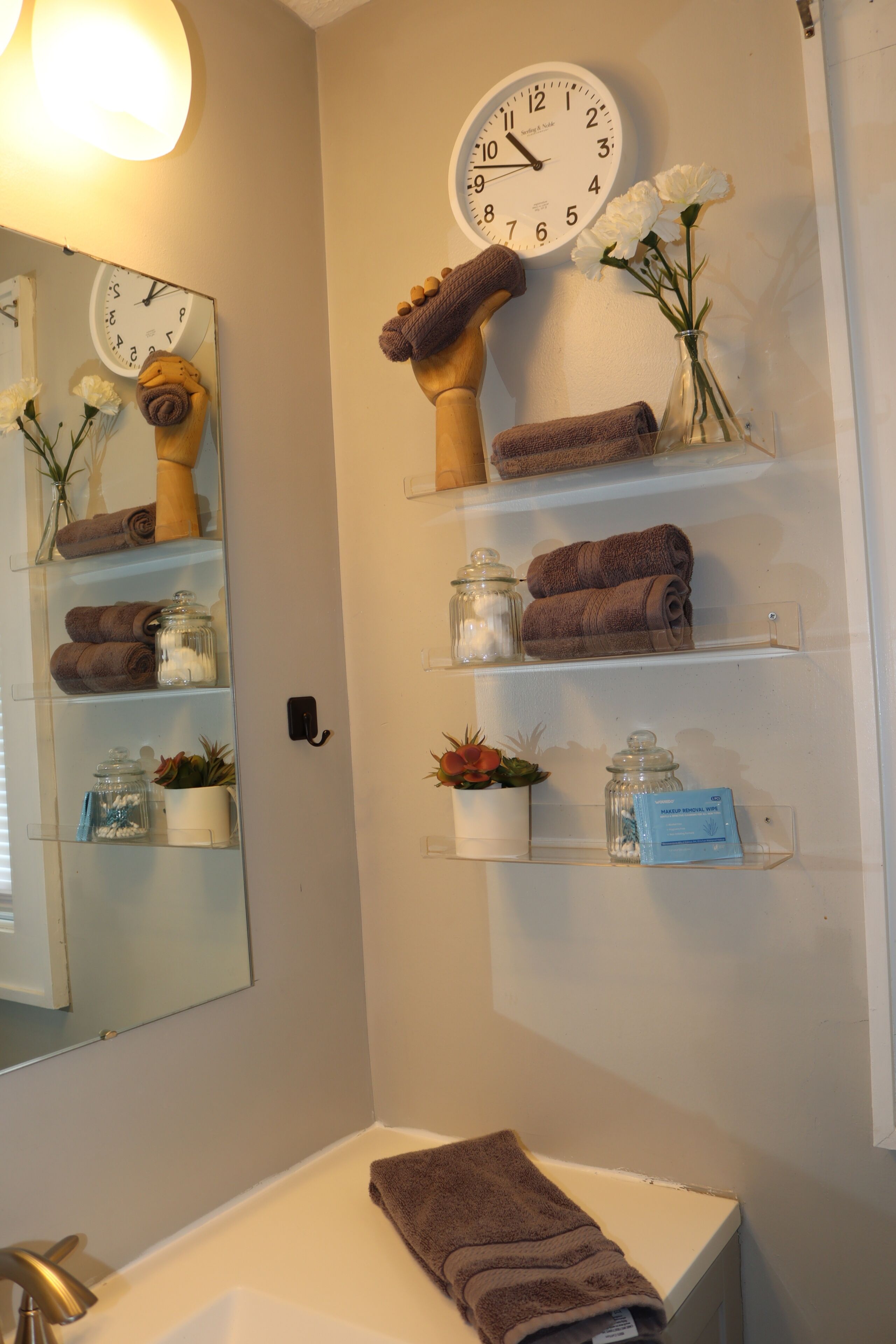 A bathroom with a white sink, a clock, and shelves with towels and toiletries.