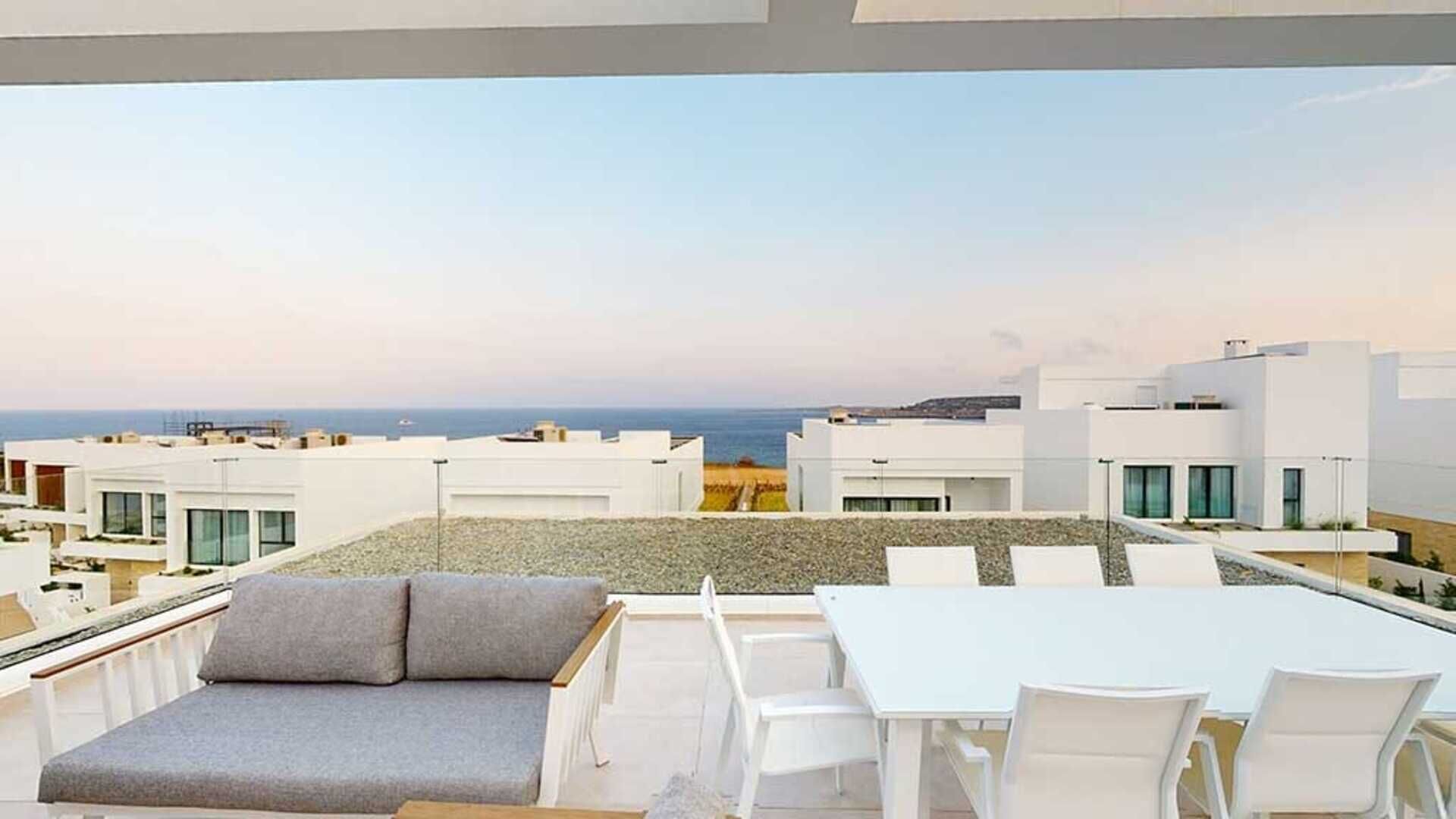 En takterrass med utsikt över havet, vita möbler och en modern arkitektonisk stil.
