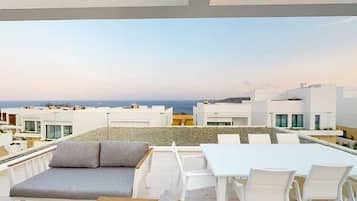 En takterrass med utsikt över havet, vita möbler och en modern arkitektonisk stil.