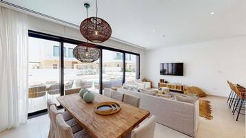 Una sala de estar moderna con una mesa de comedor de madera, sofás blancos y un ventanal con vistas a la ciudad.