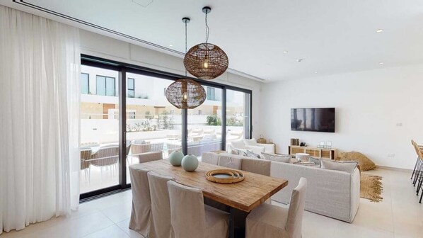 Una sala de estar moderna con comedor, ventanas grandes y televisor de pantalla plana.
