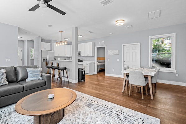 A modern living room with a gray sofa, a coffee table, and a dining area with a table and chairs. - 7 Minutes to Campus! (Gainesville)