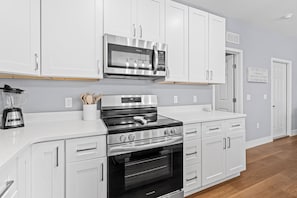 A modern kitchen with white cabinetry, stainless steel appliances, and a wooden floor. - 7 Minutes to Campus! (Gainesville)