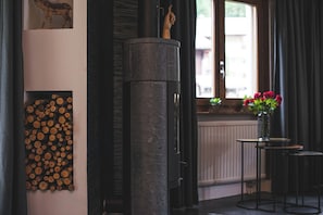 A room with a fireplace, a wall-mounted log display, a window with curtains, and a small table with a vase of flowers. - Luxury Alpine Retreat|Zermatt 1068 (Wallis)