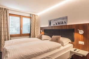 A hotel room with a large bed, a bedside table, a window with curtains, and a wall-mounted artwork. - Luxury Alpine Retreat|Zermatt 1068 (Wallis)