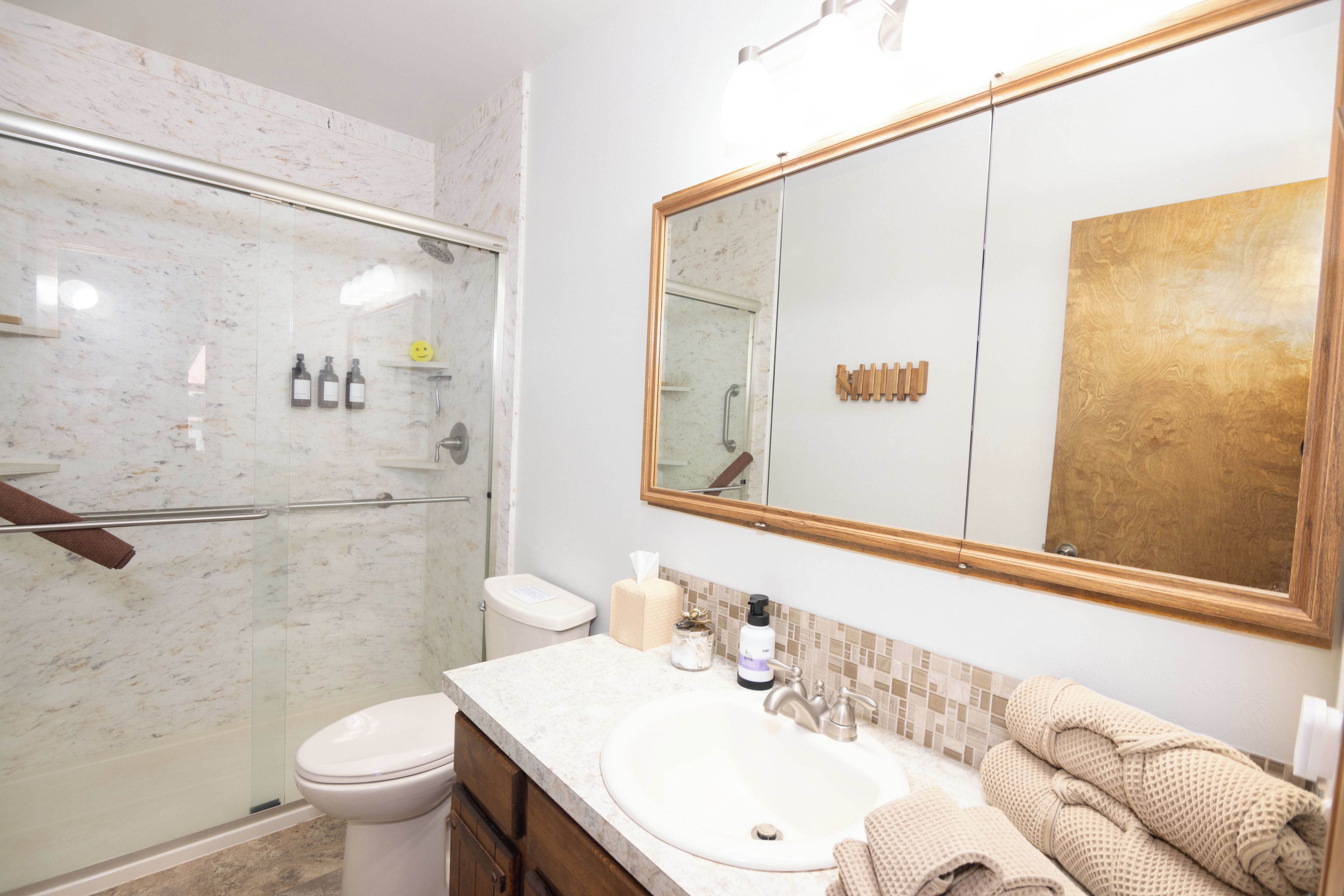 Un bagno con doccia in marmo, un water, un lavandino con uno specchio sopra e asciugamani sul ripiano.