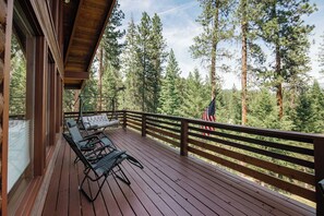 Eine Holzterrasse mit Gartenmöbeln, einem Geländer und Blick auf einen Wald mit hohen Bäumen.