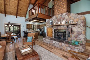 A spacious living area with a stone fireplace, wooden furniture, and a high ceiling with exposed beams. - Whispering Pines Sanctuary near Payette River & Hot Springs (Garden Valley)