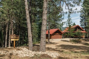 A wooden cabin with a red roof, surrounded by tall pine trees, and a sign that reads 'Welcome to Elk House.' - Whispering Pines Sanctuary near Payette River & Hot Springs (Garden Valley)