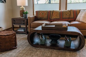 A cozy living room with a leather sofa, a wooden coffee table with magazines, a lamp, and a window with blinds. - Whispering Pines Sanctuary near Payette River & Hot Springs (Garden Valley)