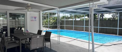 Un espacio exterior techado con piscina, una mesa con sillas y vistas al jardín trasero.