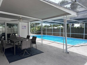 Ein überdachter Außenbereich mit Pool, Tisch und Stühlen sowie Blick auf den Garten.