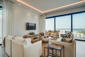 Ein modernes Wohnzimmer mit großem Fenster, einem Flachbildfernseher und Meerblick.