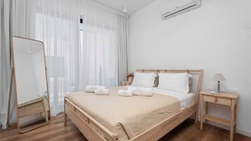 Et minimalistisk soveværelse med en træseng, hvide sengetøj, et sengebord med en lampe og en aircondition-enhed på væggen.
