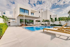 Una casa moderna amb piscina, mobiliari exterior i zona de pati coberta.
