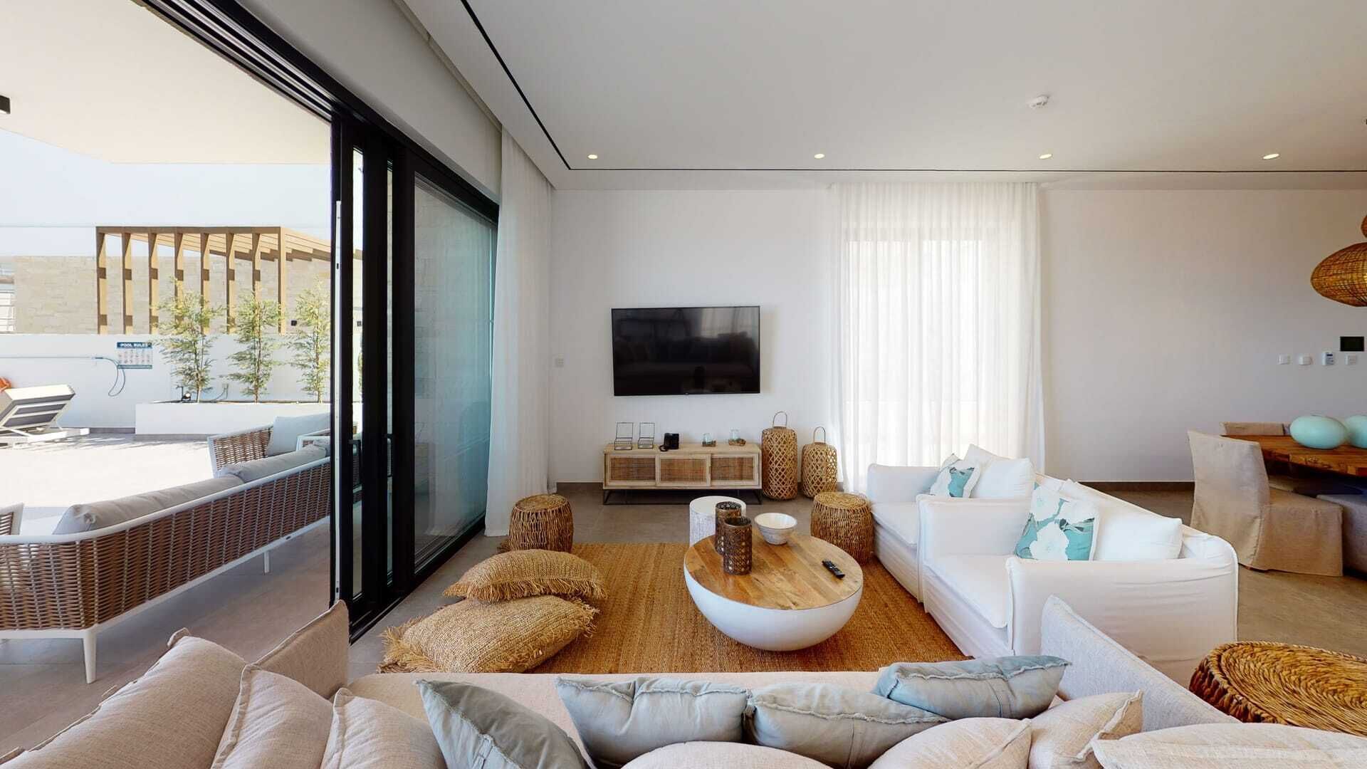 A modern living room with a large TV, white sofas, and a view of the outside.