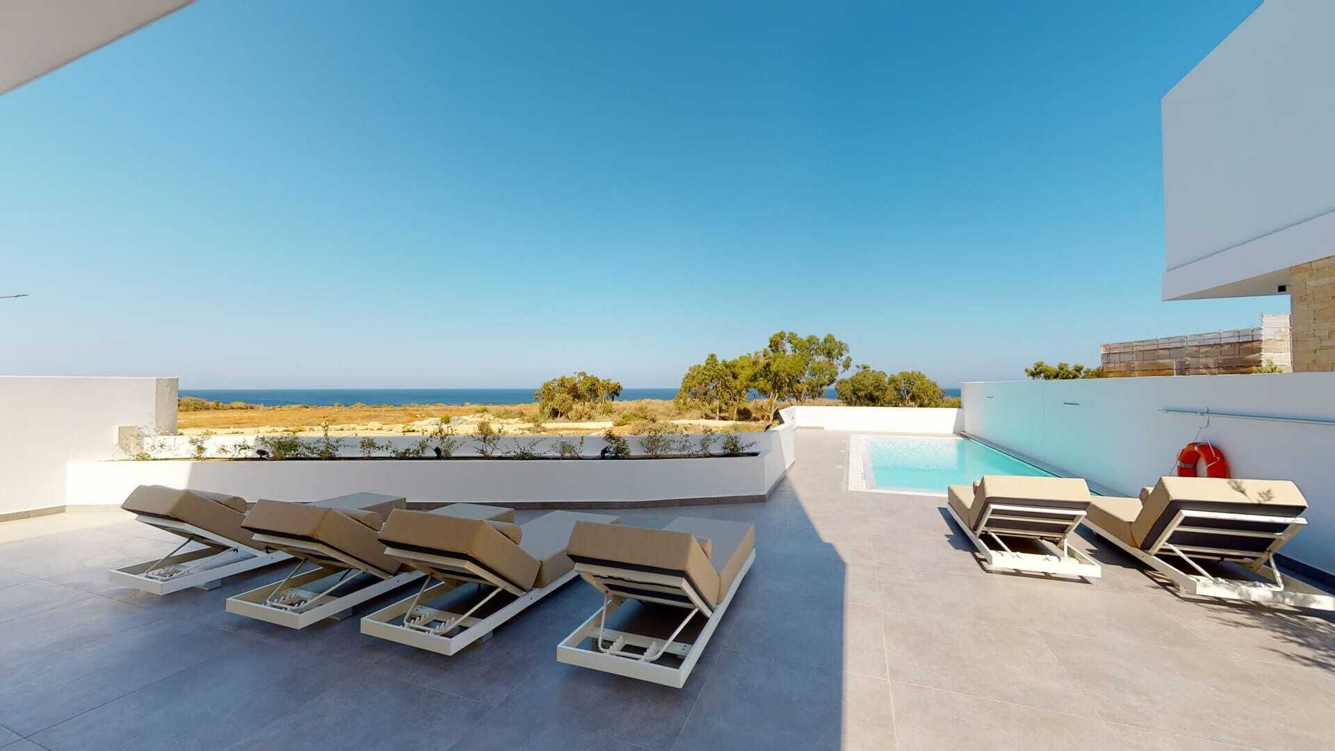 En takterrass med pool, solstolar och utsikt över havet.