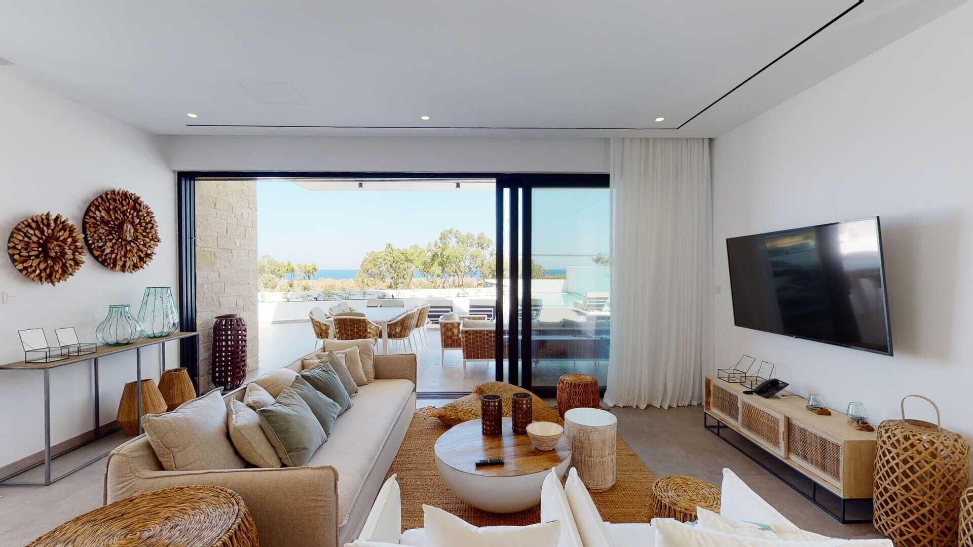 Una sala moderna con sofá, mesa de centro y televisor, con vistas a una piscina y una zona de estar al aire libre.