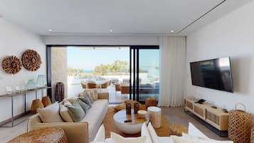 Una sala moderna con sofá, mesa de centro y televisor, con vistas a una piscina y una zona de estar al aire libre.