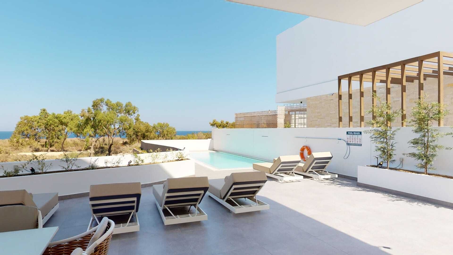A modern outdoor pool area with lounge chairs and a view of the sea.