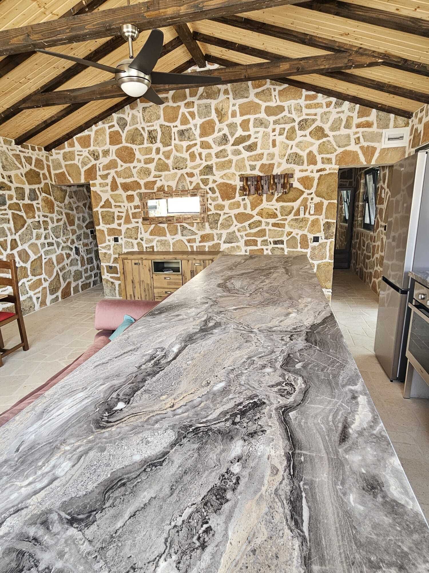Una cocina con pared de piedra, encimera de mármol y ventilador de techo.
