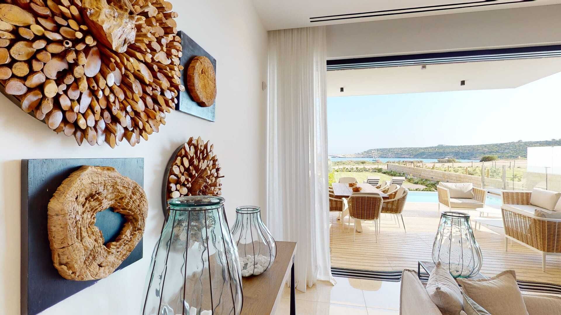 Un intérieur moderne avec vue sur la mer, comprenant un coin repas avec des meubles en osier et une table agrémentée de vases en verre.