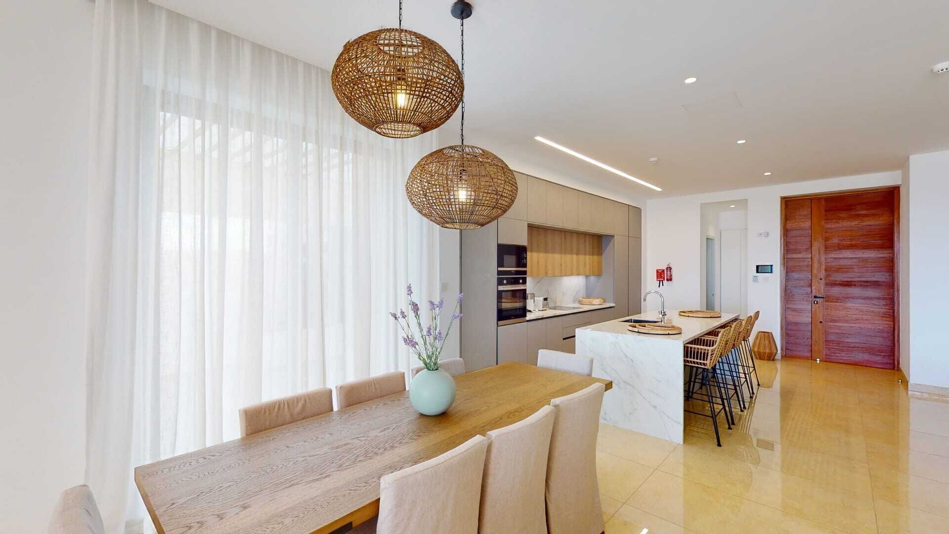 Un espace repas moderne avec une table en bois, des chaises blanches et un luminaire suspendu en rotin.