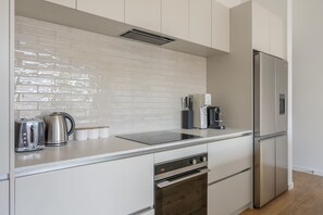 A modern kitchen with white cabinetry, a stainless steel refrigerator, a built-in oven, and a coffee maker. - The Lookout, BBQ, Free Parking, AC, Heating (Lake Hayes Estate)