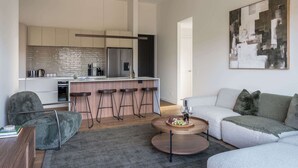 Ein modernes Wohnzimmer mit einem grauen Sofa, einem runden Couchtisch mit Früchten und einer Küche im Hintergrund.