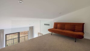Ein modernes Wohnzimmer mit einem braunen Sofa, einer Glastrennwand und Blick auf einen Balkon.
