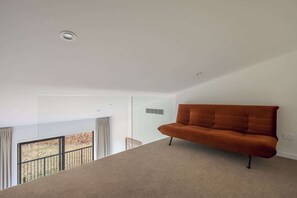 Ein modernes Wohnzimmer mit einem braunen Sofa, einer Glastrennwand und Blick auf einen Balkon.