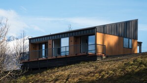 Ein modernes, zweistöckiges Haus mit Balkon, Holzfassade und großen Fenstern.