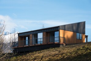 Ein modernes, zweistöckiges Haus mit Balkon, Holzfassade und großen Fenstern.