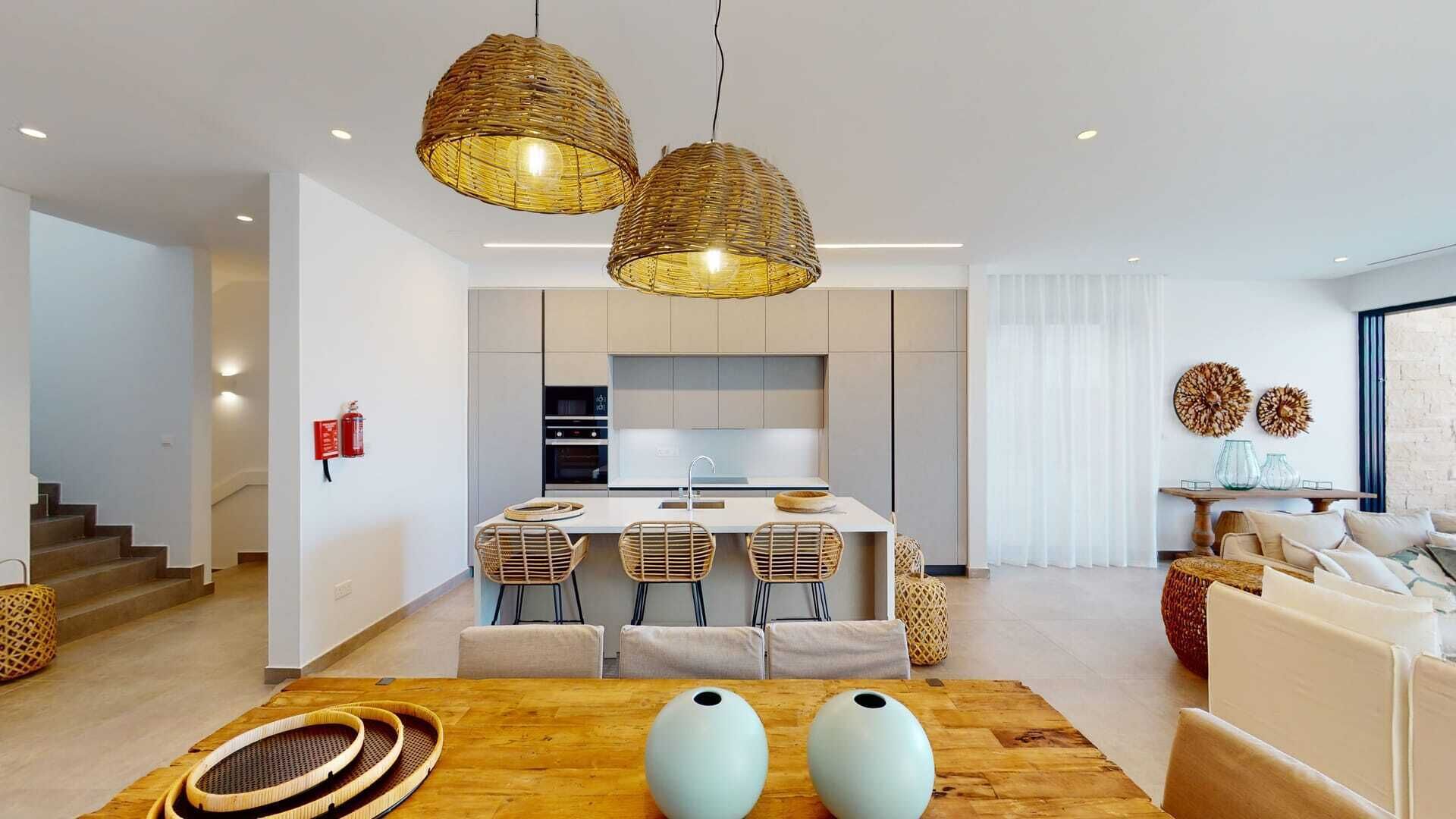 A modern kitchen with a central island, two hanging wicker pendant lights, and a dining area with a wooden table and woven chairs.