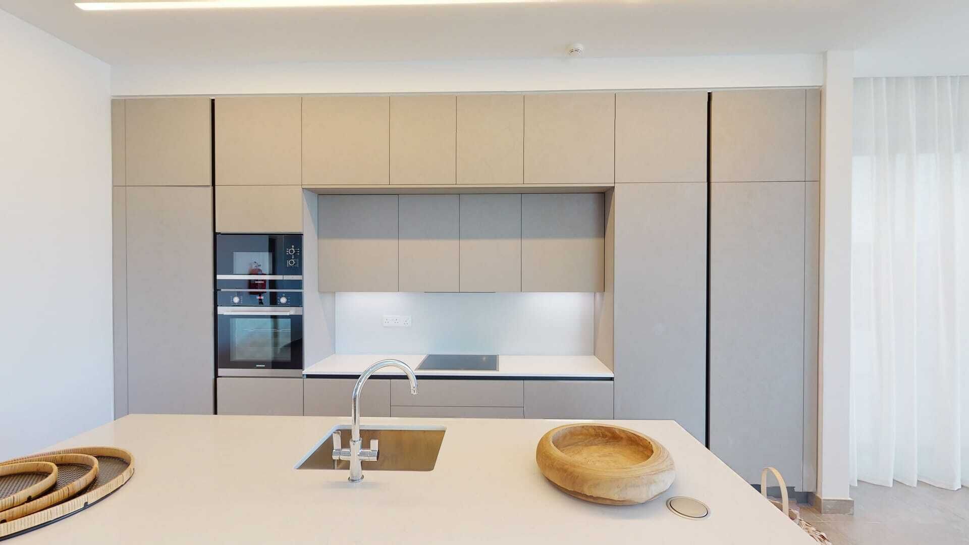 A modern kitchen with a central island, built-in oven, and a large window.