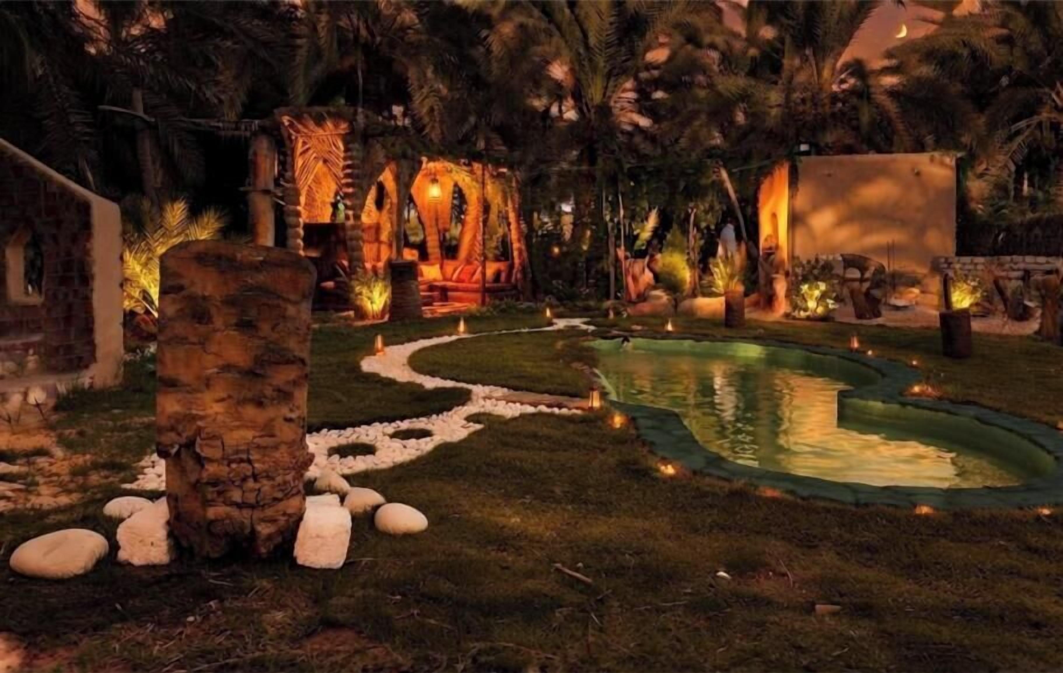 Un giardino curato con piscina, elementi in pietra e illuminazione soffusa.