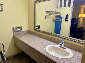 Une salle de bain dotée d’un comptoir en granit, d’un lavabo blanc, d’un miroir avec un cadre décoratif, d’un distributeur de serviettes et d’un porte-serviettes avec des crochets.