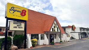 Et Super 8 motel med rødt tag, et skilt der angiver priser for hospitaler, offentlige tjenestemænd og ARP, samt en parkeringsplads.