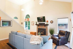 Ein Wohnzimmer mit Kamin, einer Couch, einem Ledersessel, einem Fernseher und einer Treppe.